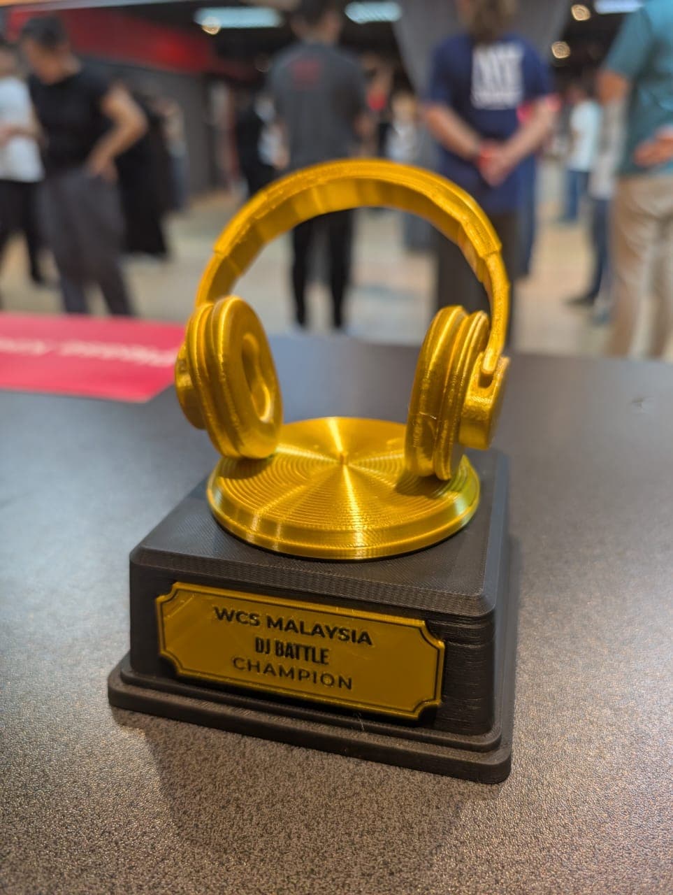 A 3D printed gold headphone trophy on a black plinth engraved WCS Malaysia DJ Battle Champion