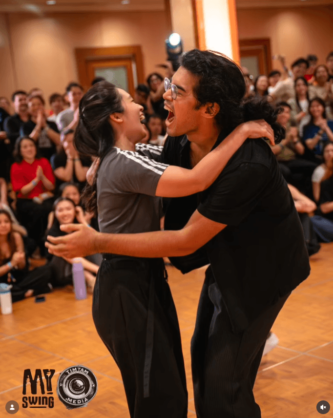 Ashraff mid-routine on a social dance floor with a partner, surrounded by a seated crowd