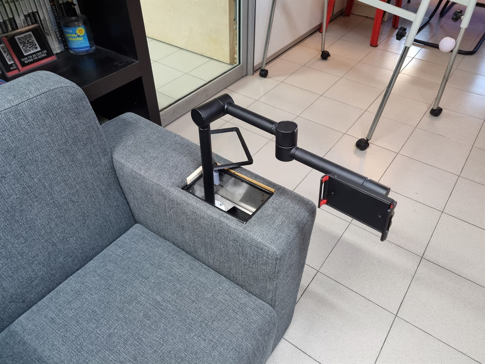 An articulated black device holder arm extending out of a grey couch armrest